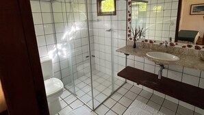 A bathroom with a glass shower enclosure, a toilet, a sink with a marble countertop, and a mirror with a floral frame. - Pousada Villa Cumuru (Prado)