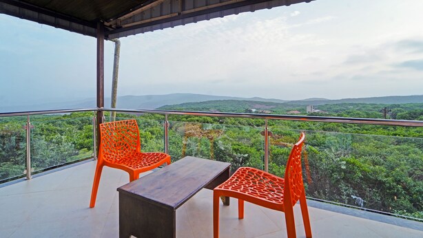 A balcony with two orange chairs and a wooden table, overlooking a lush green landscape. - Treebo Shindola Resort (Mahabaleshwar)