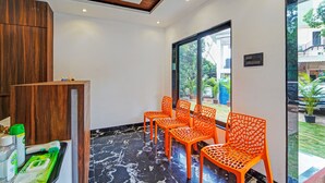 A room with a wooden cabinet, a reception desk, and orange chairs arranged near a large window. - Treebo Shindola Resort (Mahabaleshwar)