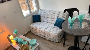 Een knus vertrek met een gestreept bankje, een tafeltje met blauwgroene objecten, en een bank met een hoed en een lantaarn.