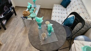 Een gezellige zithoek met een ronde tafel voor twee personen, een bank met gestreepte kussens, en een televisie op een meubel.