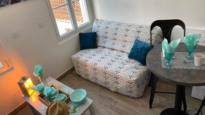 Een knus interieur met een gestreept bankje, een klein tafeltje met decoratieve objecten en een raam met uitzicht.