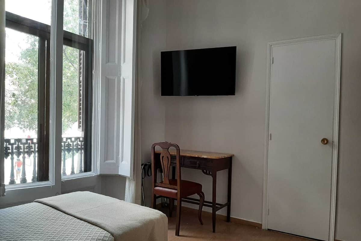A room with a bed, a desk, a chair, a television, and a door.