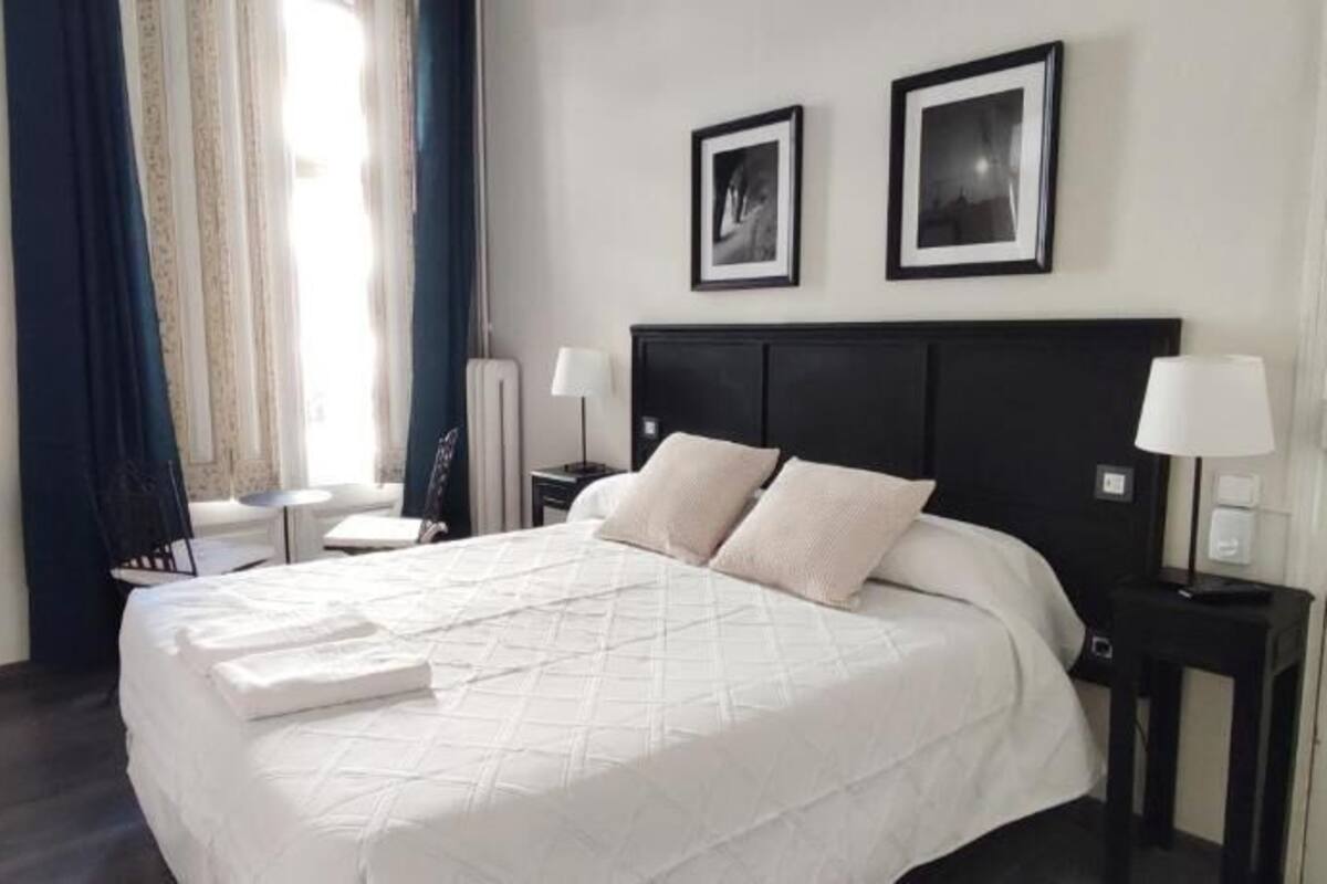 A neatly made bed with a white quilt, a bedside table with a lamp, and a wall-mounted mirror.