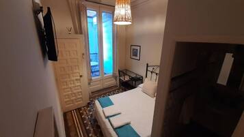 Habitación de hotel con cama, una mesita, una silla, una puerta y vistas al exterior.