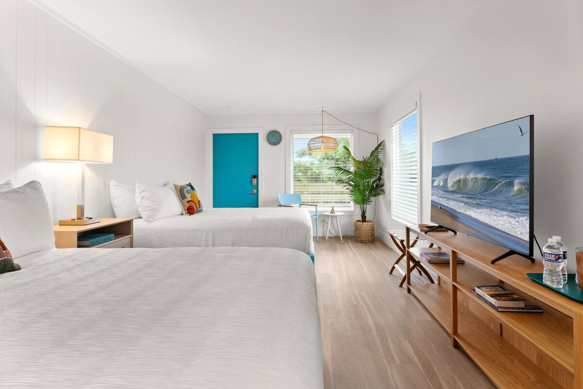 A hotel room with two beds, a TV, a desk, and a view of the ocean.