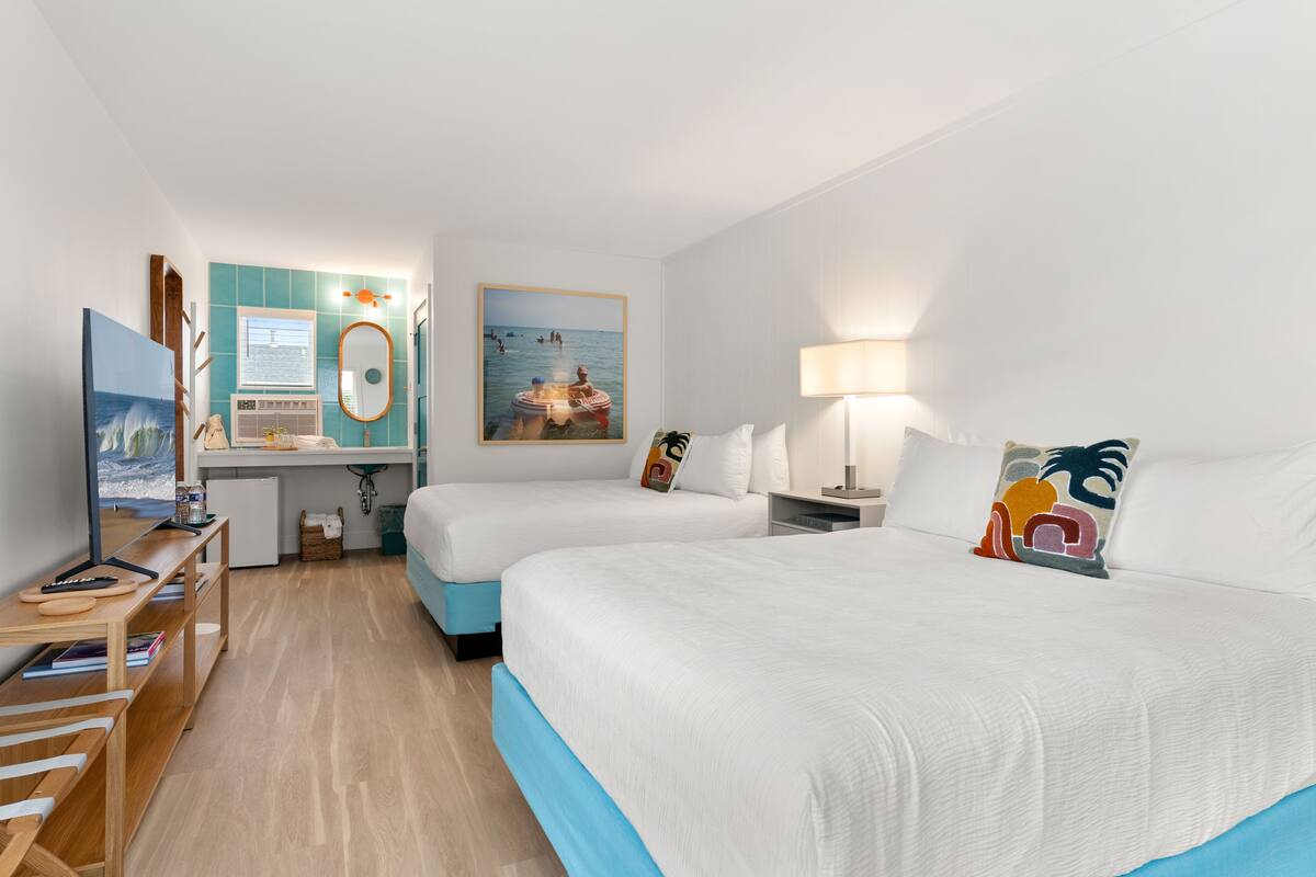 A hotel room with two beds, a desk with a computer, a TV, and a window with a view of the sea.