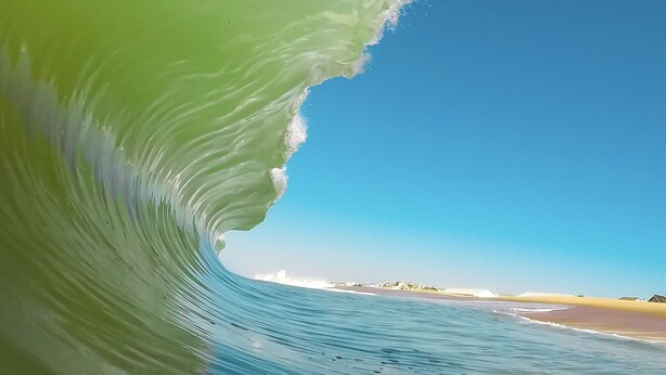 A wave curling over a beach with a clear sky in the background. - The Surf Shanty Motel (Dewey Beach)