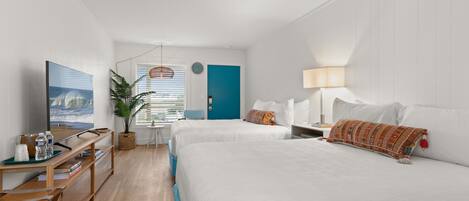A hotel room with two beds, a desk with a computer, a TV, and a window with a view of the beach.