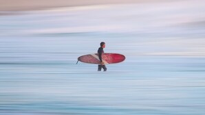 A person walking on a beach with a surfboard. - The Surf Shanty Motel (Dewey Beach)