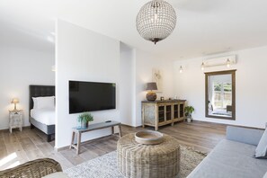 Una sala moderna con una cama, un televisor de pantalla plana, un sofá, un taburete de mimbre, una mesita y una lámpara.