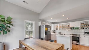 Una cucina moderna con mobili bianchi, un'isola centrale, elettrodomestici in acciaio inossidabile e un'ampia finestra.
