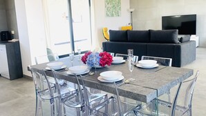 Un comedor moderno con una mesa de vidrio, sillas transparentes y un sofá gris al fondo.
