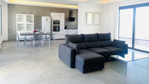 Una sala de estar moderna con un sofá modular, una mesa de centro de vidrio y una zona de comedor con un aparador blanco y sillas transparentes.