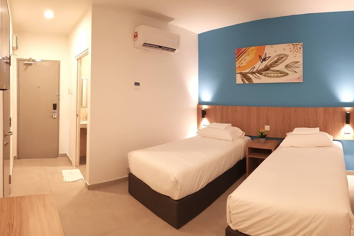 A hotel room with two beds, a wooden headboard, a wall-mounted air conditioner, and a painting.