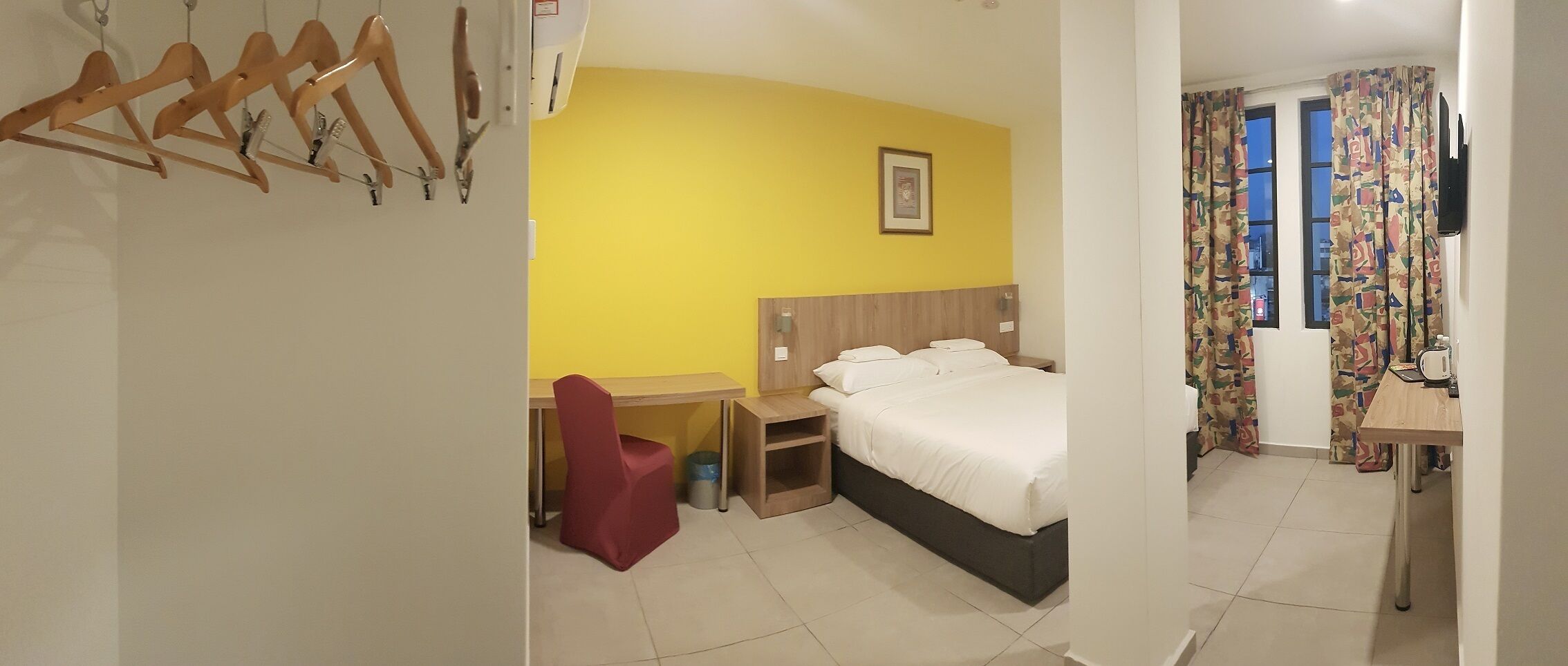 A hotel room with a bed, a desk, a chair, and a wardrobe.