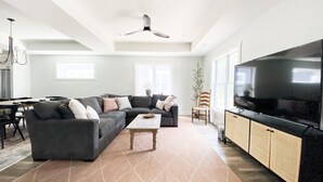 A spacious living room with a sectional sofa, a coffee table, a TV, and a dining area with a table and chairs. - Modern New-Build w/ Screened Porch - Walk to Beach (Michigan City)