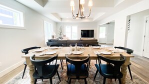 A dining area with a large wooden table set for six, surrounded by black chairs. A chandelier hangs from the ceiling, and a television is mounted on the wall in the background. - Modern New-Build w/ Screened Porch - Walk to Beach (Michigan City)