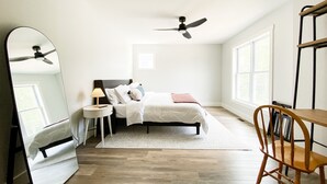 A bedroom with a bed, a ceiling fan, a bedside table with a lamp, a chair, and a large mirror. - Modern New-Build w/ Screened Porch - Walk to Beach (Michigan City)