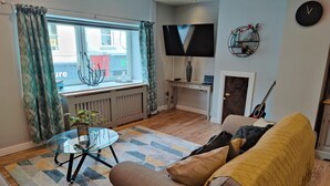 A living room with a sofa, a glass coffee table, a TV, a guitar, and a window with curtains. - NEW Fabulous 2BD Maisonette Dunfermline, Fife (Dunfermline)