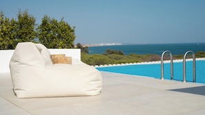 Un sillón de mimbre blanco junto a una piscina con vista despejada al océano.