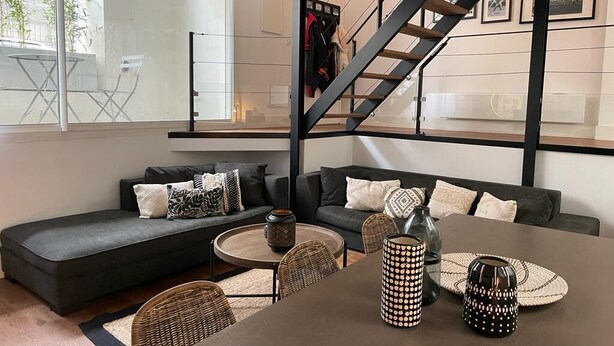A modern living room with a dark sofa, a round coffee table, and a staircase. - Magnificent 4* apartment, ideally located (Biarritz)