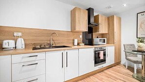 A modern kitchen with white cabinets, a wooden countertop, a stainless steel sink, a microwave, and an oven. - Luxury One Bed Apartment -  Jewellery Quarter (Birmingham)