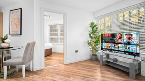 A modern living room with a flat-screen TV displaying movie options, a dining area with a glass table and chairs, a potted plant, and a framed artwork on the wall. - Luxury One Bed Apartment -  Jewellery Quarter (Birmingham)