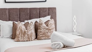 A neatly made bed with a white and beige blanket, a brown headboard, and several pillows. - Luxury One Bed Apartment -  Jewellery Quarter (Birmingham)