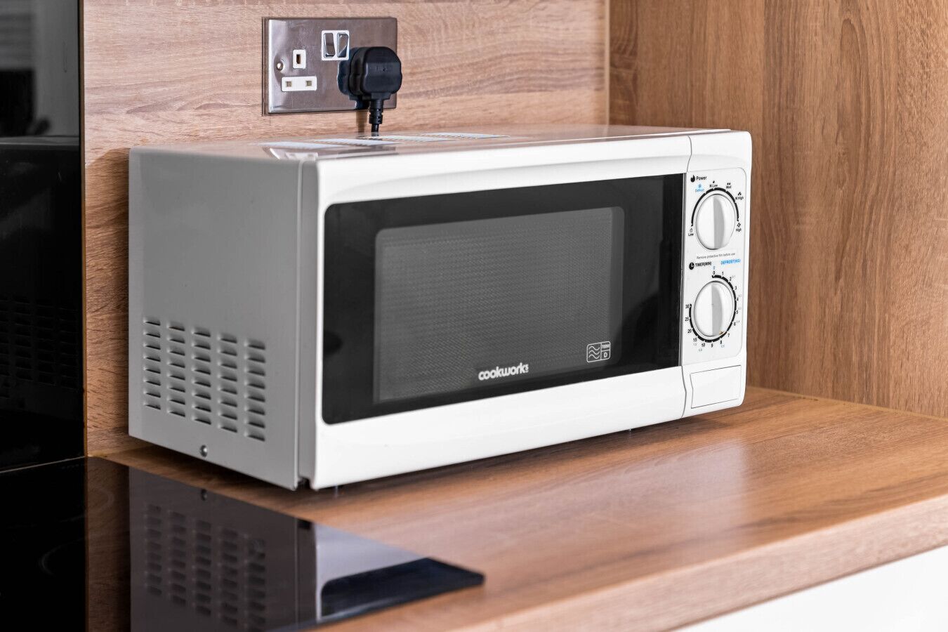 Un four à micro-ondes compact, doté d’un panneau de commande noir, posé sur un plan de travail en bois.