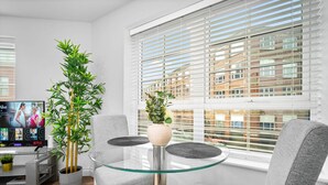 Una sala de estar moderna con una mesa de vidrio, sillas grises, una planta en maceta y un televisor mostrando la interfaz de Netflix.