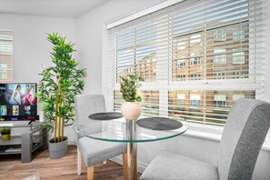 Ein modernes Wohnzimmer mit Glastisch, grauen Sesseln, einer Topfpflanze und einem Fernseher, der eine Netflix-Oberfläche zeigt.