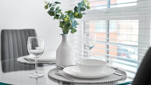 Een eettafel met een witte vaas, een glas en een kom op een glazen tafel.