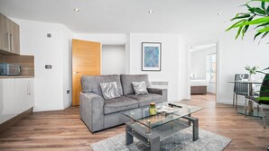 Een moderne woonkamer met een grijze bank, een glazen salontafel en een houten deur.