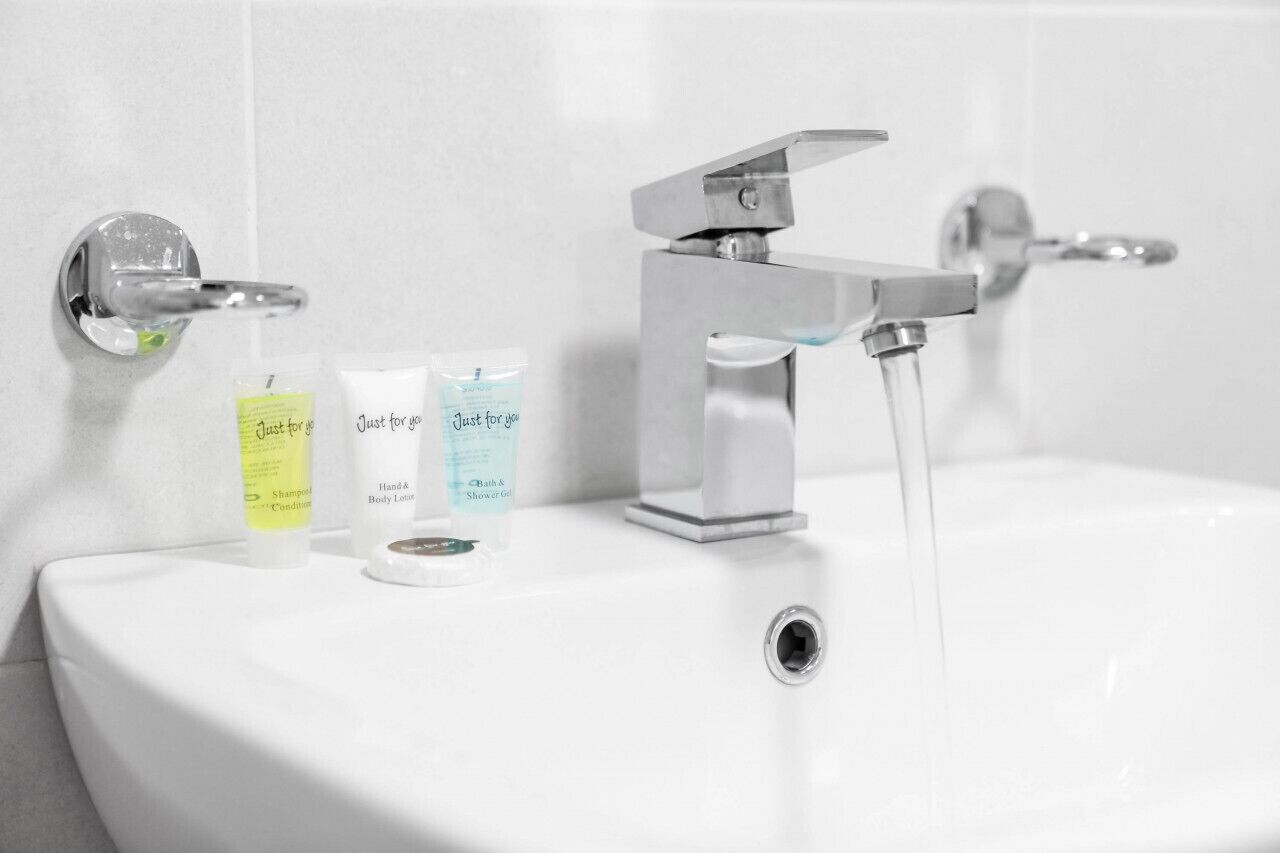 Een badkamermeubel met een wastafel, twee flessen hand- en bodylotion en een fles shampoo.