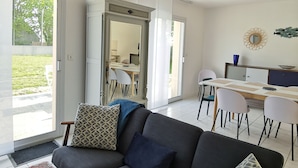 A modern living room with a grey sofa, patterned cushions, a large rug, and a dining area with a table and chairs.