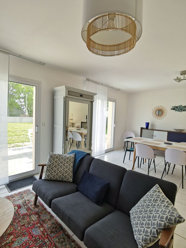 A modern living room with a grey sofa, patterned cushions, a large rug, and a dining area with a table and chairs.