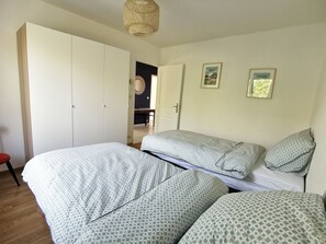 A bedroom with two beds, a wardrobe, and a door leading to another room.