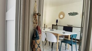 A dining area with a white table and chairs, a decorative wall hanging, and a view through a large window.
