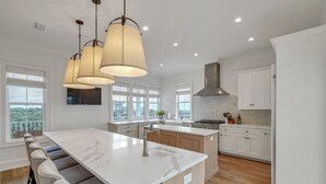 A modern kitchen with a large island, white cabinetry, and pendant lighting.