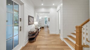 A hallway with white walls, wooden flooring, a staircase with wooden railings, and a door with glass panels.