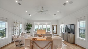 A spacious living room with a high ceiling, large windows, and a modern chandelier.