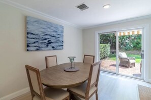 Enjoy meals in this cozy dining area with a round table and comfortable chairs, surrounded by a beautiful abstract art piece and sliding glass door leading to a serene outdoor patio.