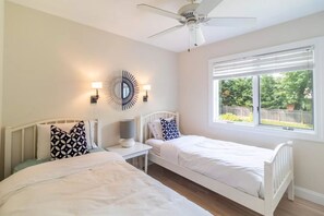 Two single beds with white headboards and matching pillows, a ceiling fan, and a wall-mounted mirror.