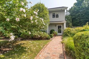 Stroll up the brick pathway to this charming two-story home with a modern architectural style and lush green surroundings.