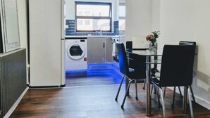 A compact kitchen with a washing machine, a dining area with two chairs, and a window providing natural light. - Beautiful & Clean 1 bed Apartment in Hackney Wick (London)