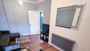 A modern living room with a glass-top dining table, a sofa, a TV, and a decorative mirror. - Beautiful & Clean 1 bed Apartment in Hackney Wick (London)