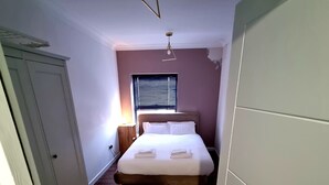 A bedroom with a bed, a nightstand, a window with blinds, and a ceiling light fixture. - Beautiful & Clean 1 bed Apartment in Hackney Wick (London)
