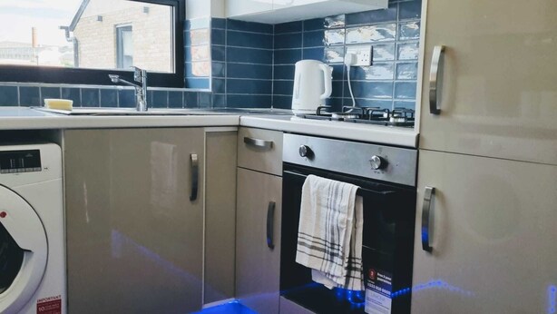 A compact kitchen with a washing machine, a stove, and a window overlooking a brick building. - Beautiful & Clean 1 bed Apartment in Hackney Wick (London)