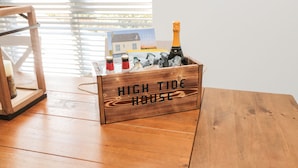 A wooden crate labeled "HIGH TIDE HOUSE" with a bottle of champagne and a postcard.
